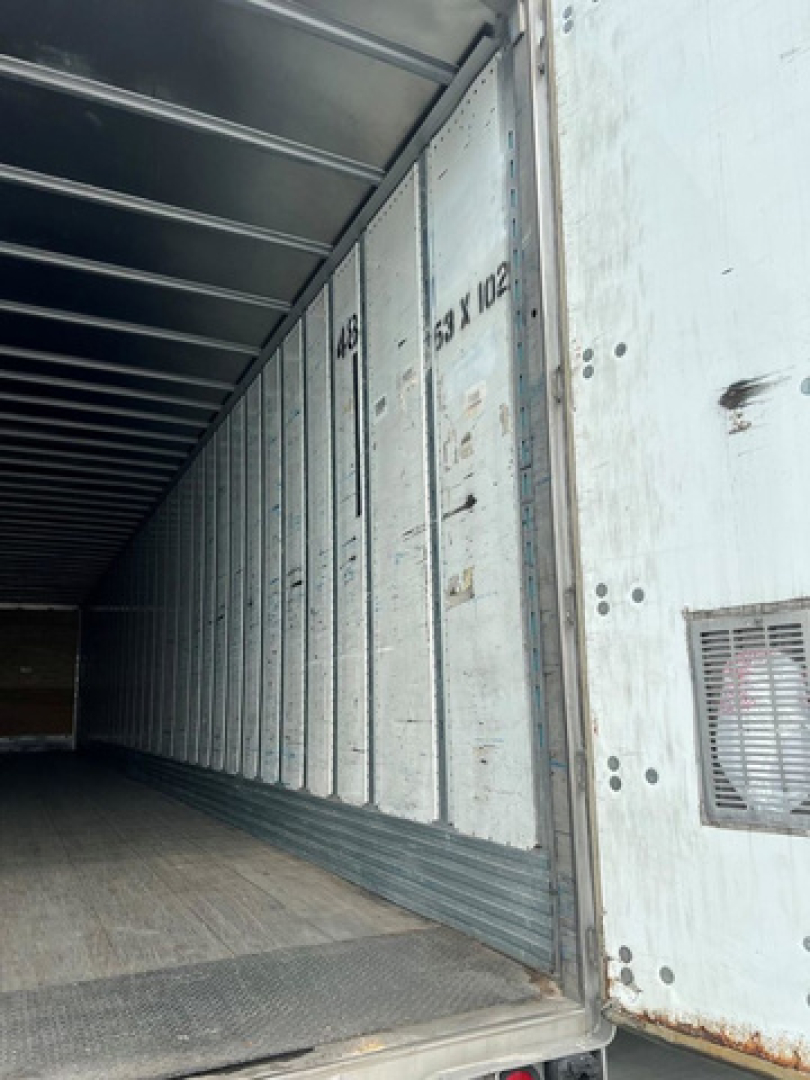 Trailer interior showing cargo bay with ribbed metal walls and a sliding door frame; visible numbers stamped on panel and a small vent on right side.