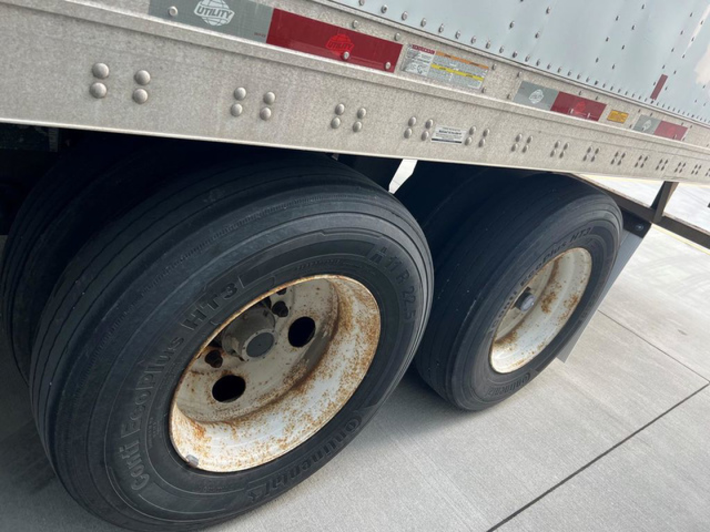 Trailer wheels with dual tires mounted under a utility van trailer; visible rust on wheel rims and tread details.