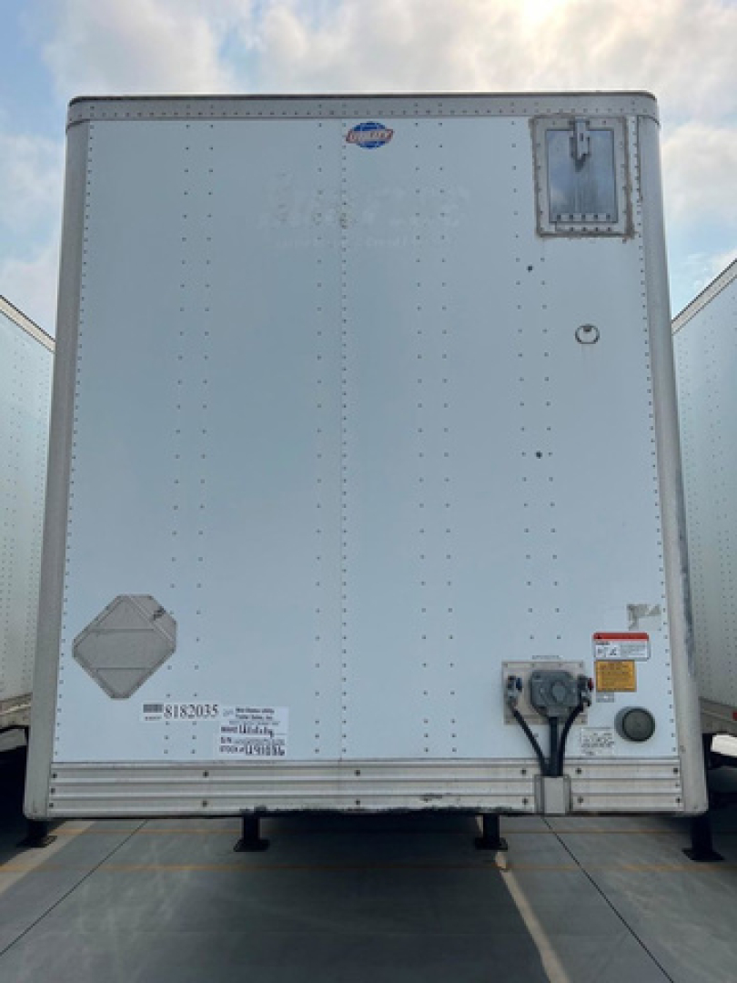 Rear view of a white utility trailer van with riveted metal walls, repair access hatch, vents, and a trailer hitch area.
