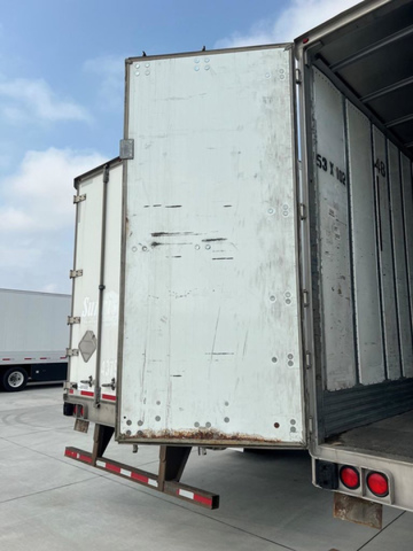 Trailer rear door of a utility van showing weathered metal surface, visible hinges, and lower rear bumper with reflective tape.