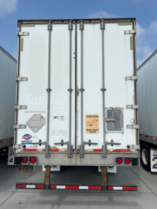 Rear view of a white cargo trailer with closed double doors and multiple latches.