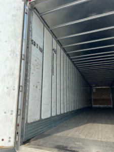 Interior of a box truck trailer showing tall side panels with numbers 53 10? 48 etc and a wooden floor; cargo area empty.