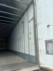 Trailer interior showing cargo bay with ribbed metal walls and a sliding door frame; visible numbers stamped on panel and a small vent on right side.