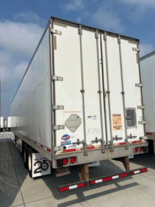 Rear view of a white utility van trailer showing doors and tail lights with decals and warning labels.