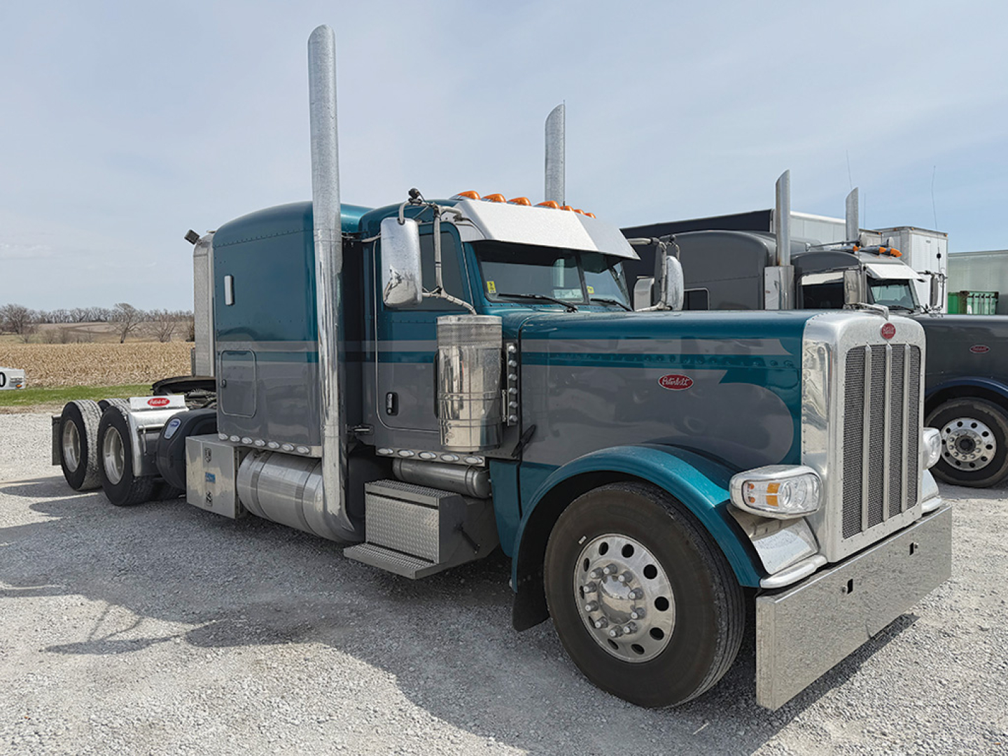 Peterbilt 389 extended hood conventional sleeper truck showing chrome exhaust stacks and blue/gray paint.