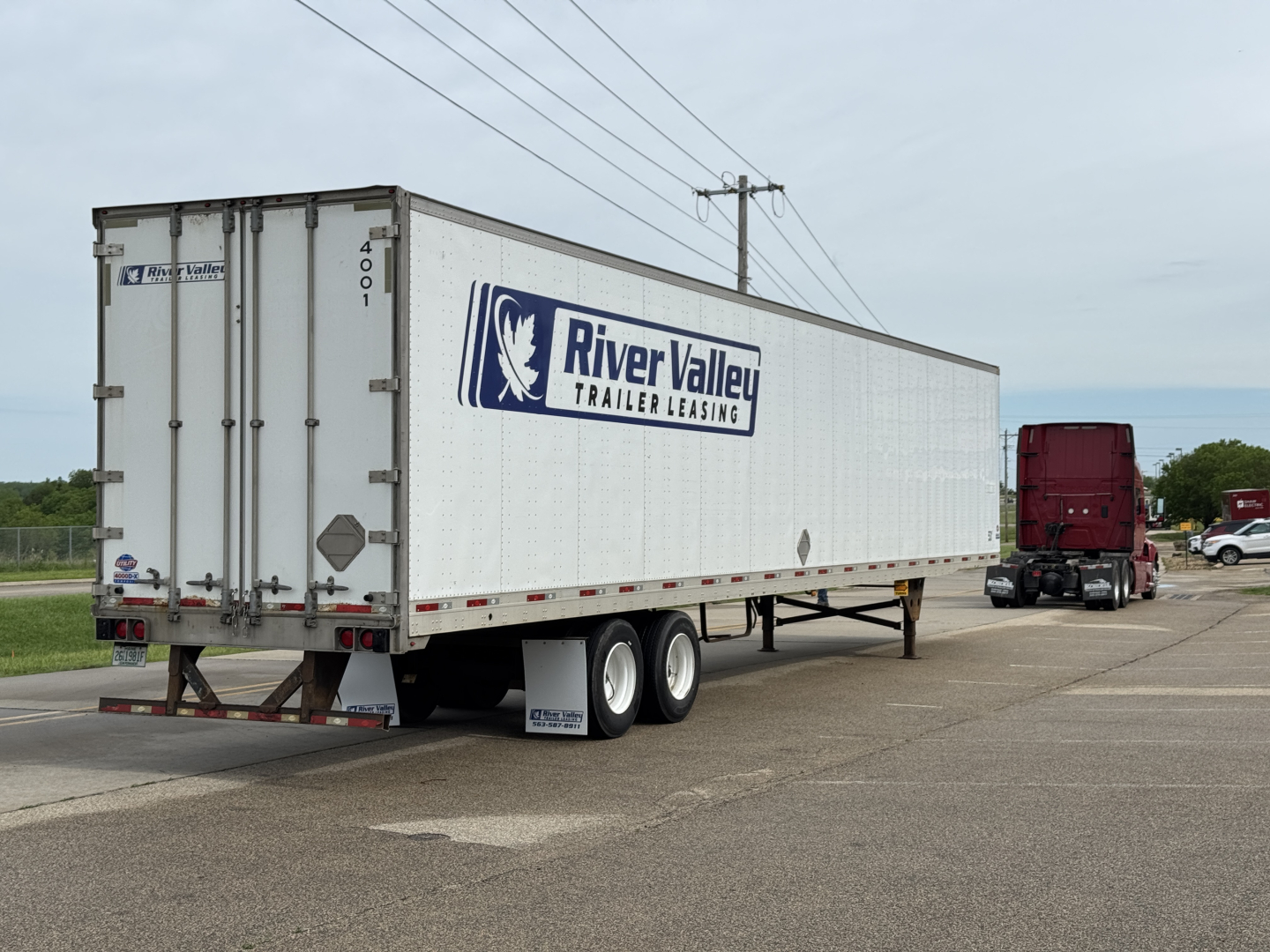 Large white River Valley trailer with blue logo and text, attached to a red semi-truck, in a parking lot. Side of trailer shows River Valley Trailer Leasing branding.
