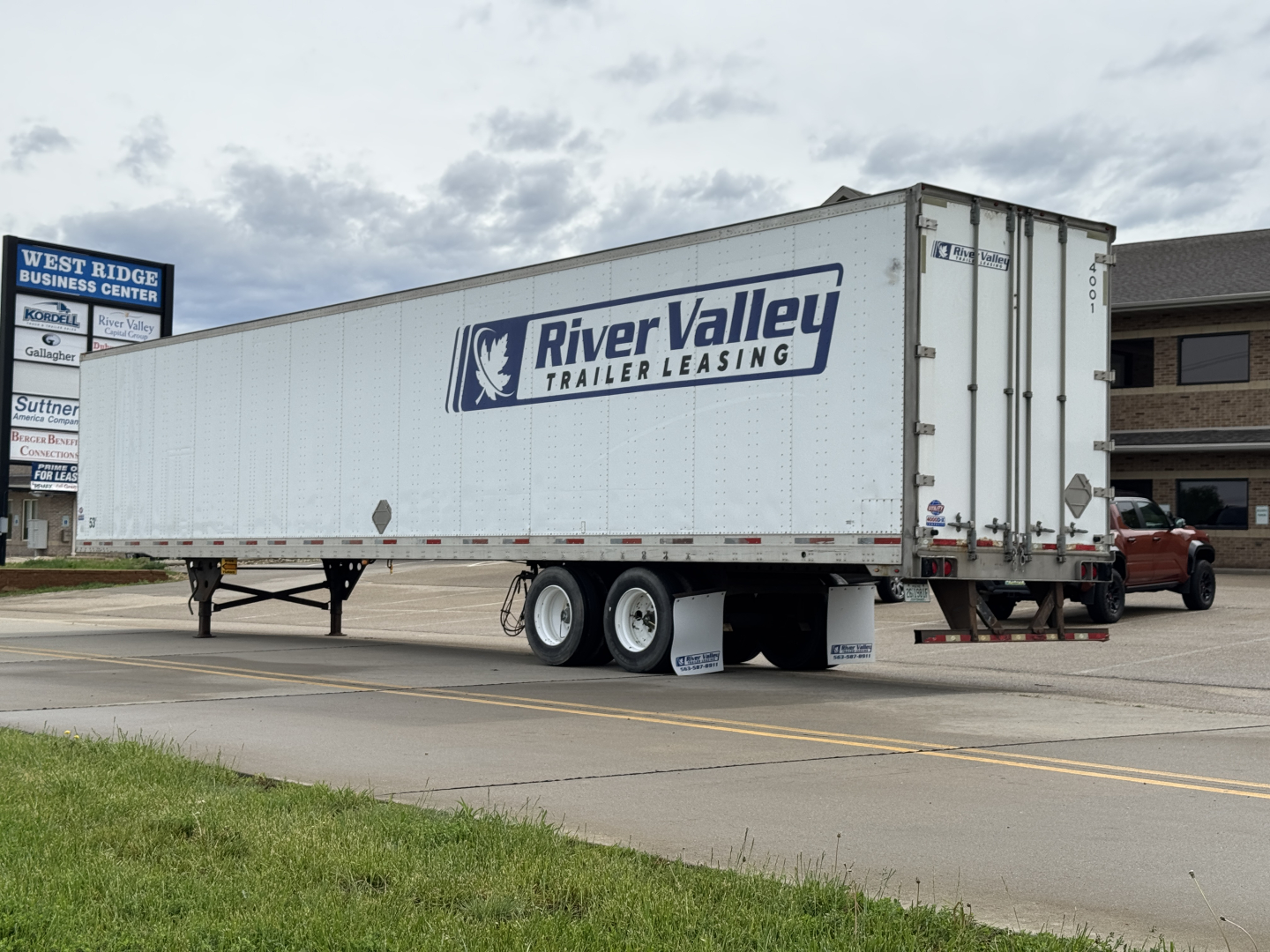 Trailer showing River Valley Leasing logo on a white utility trailer with dual rear wheels and a raised landing gear, in a parking lot.