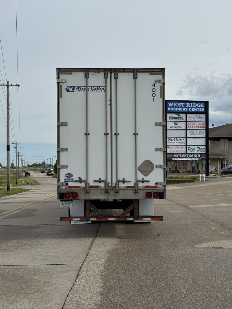 Rear view of a white utility trailer with double doors and River Valley logo, tail lights, bumper, and a 4001 number on the right door.