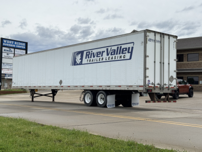 Trailer showing River Valley Leasing logo on a white utility trailer with dual rear wheels and a raised landing gear, in a parking lot.