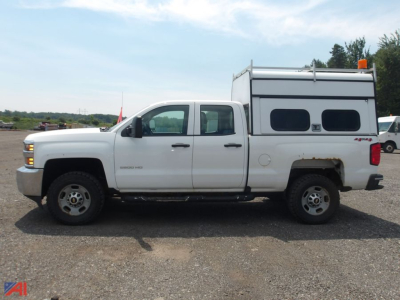2018 Chevrolet Silverado 2500HD quad cab pickup truck with white utility cap parked on gravel; side profile view; badge reads 2500 HD on front door; 4x4 badge on rear quarter; marker lights on cab roof