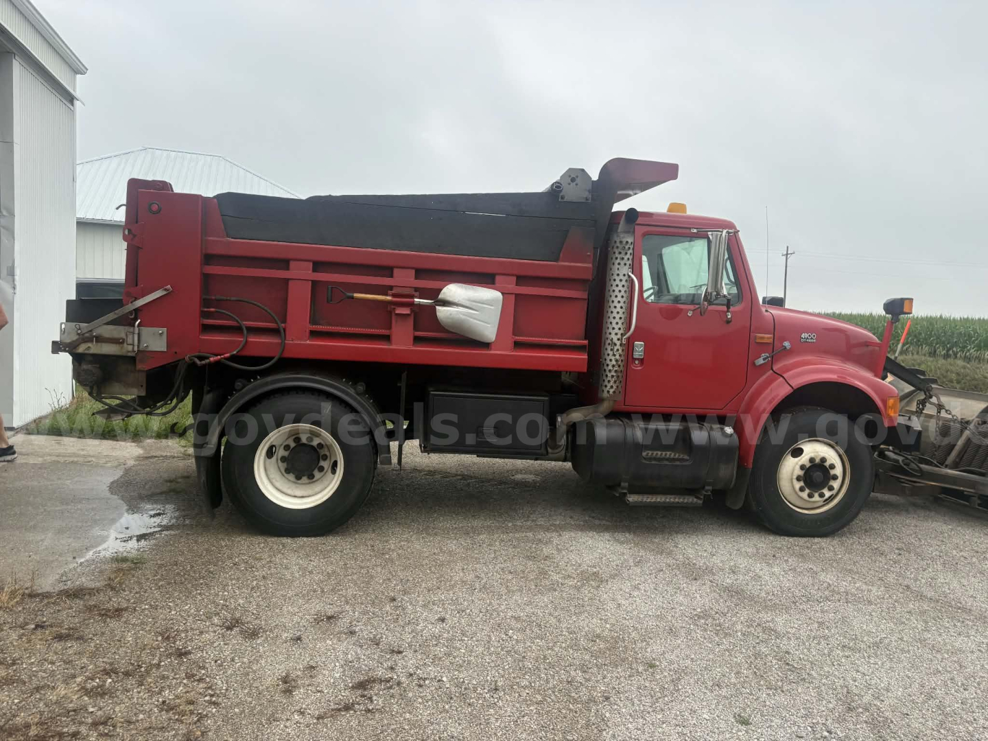 Dump truck side view showing red International 4900 dump bed with black tarp cover, dual rear wheels, and VIN/stock area not visible