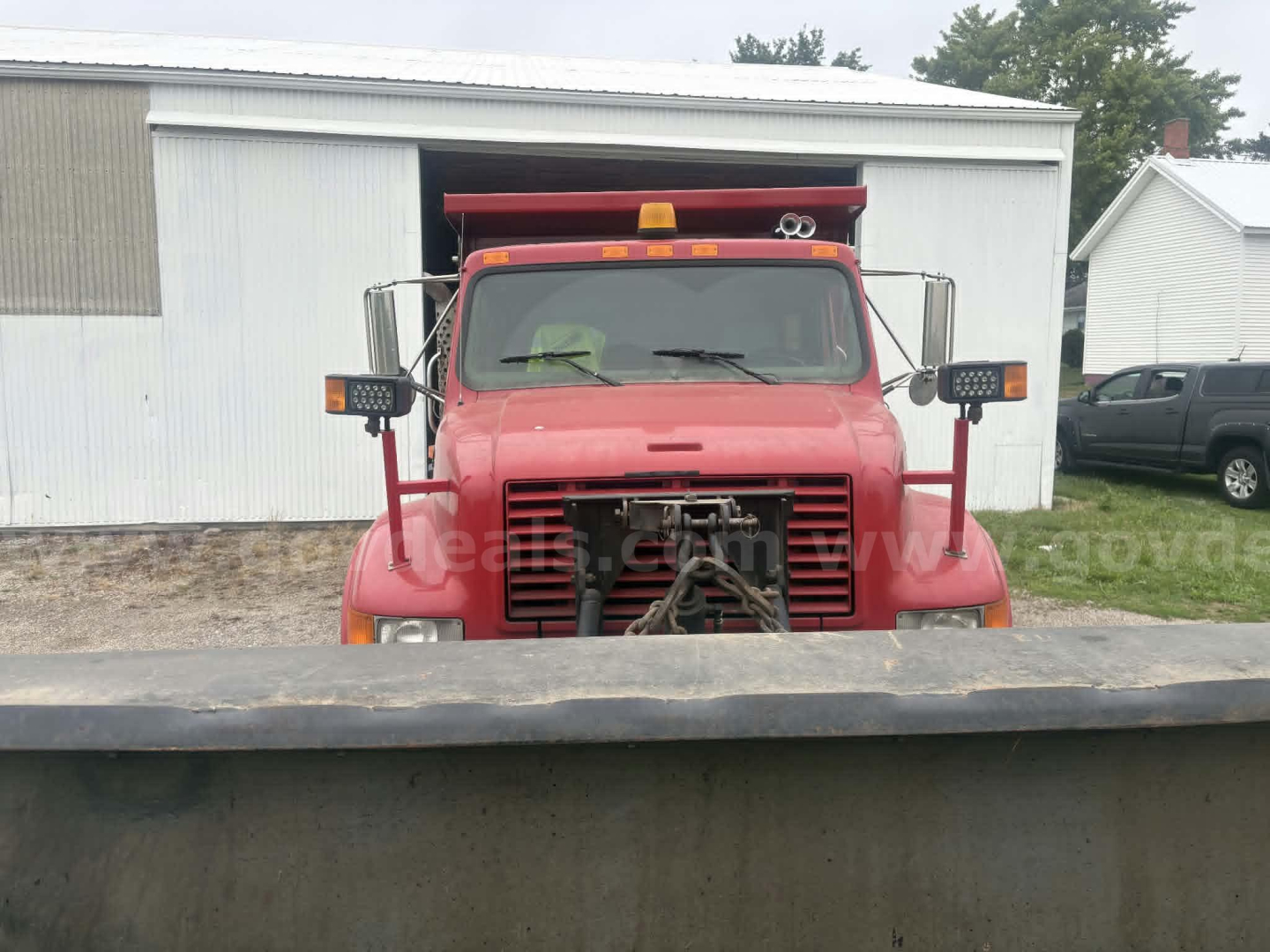International 4900 dump truck front view showing grille and bumper, red cab, side mirrors, and light bar.