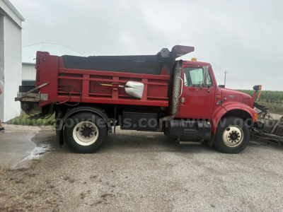 Dump truck side view showing red International 4900 dump bed with black tarp cover, dual rear wheels, and VIN/stock area not visible