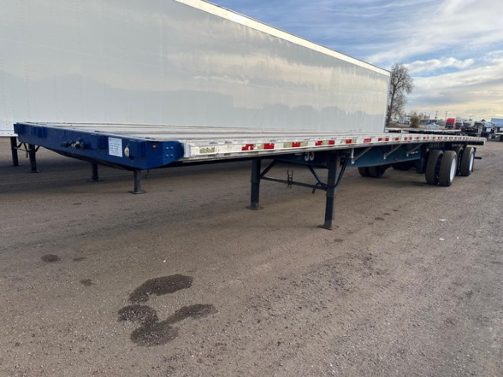 Flatbed trailer in serviceable condition showing tandem axle with dual tires and support legs, blue frame and white dry van body, reflective tape along sides.
