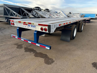 Flatbed trailer showing dual rear axles and blue safety underride guard with Air Ride branding on rear bumper. Extended aluminum deck with metal frame and reflectors.