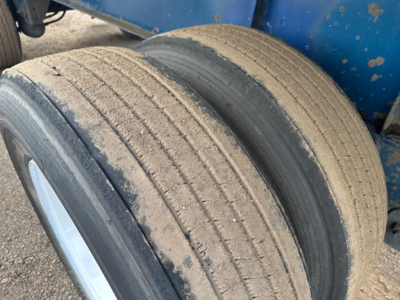 Great Dane trailer wheel and frame showing dual tires with dirt; blue trailer body in background.