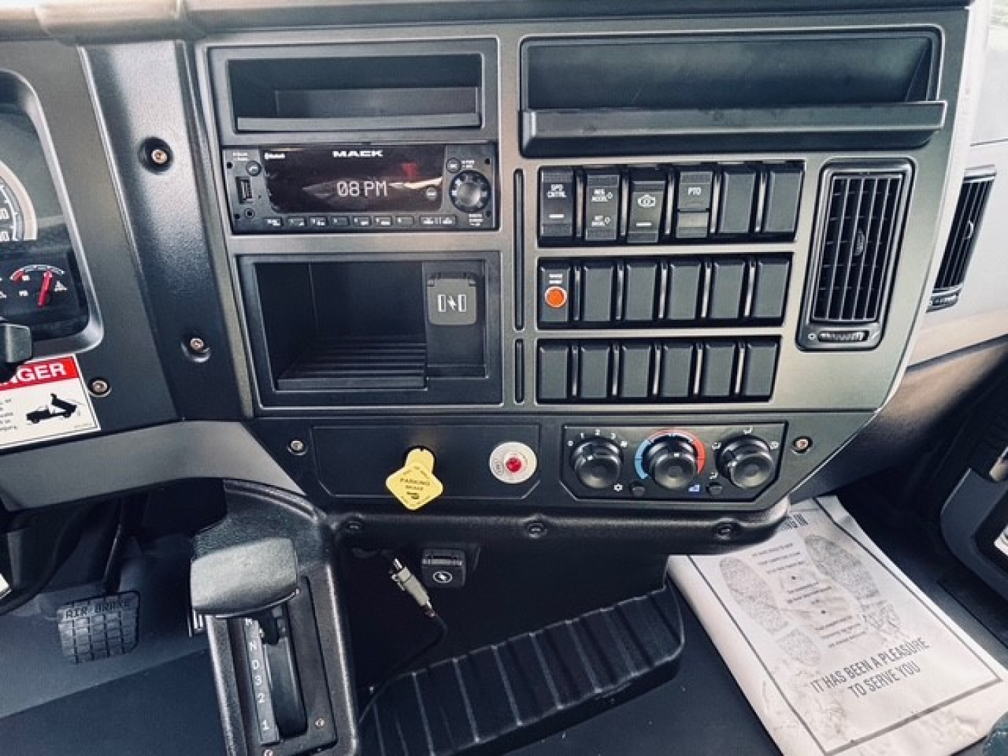 Dashboard and center console of a 2025 Mack MD6 dump truck showing radio, climate controls, switches, and an idle key area.