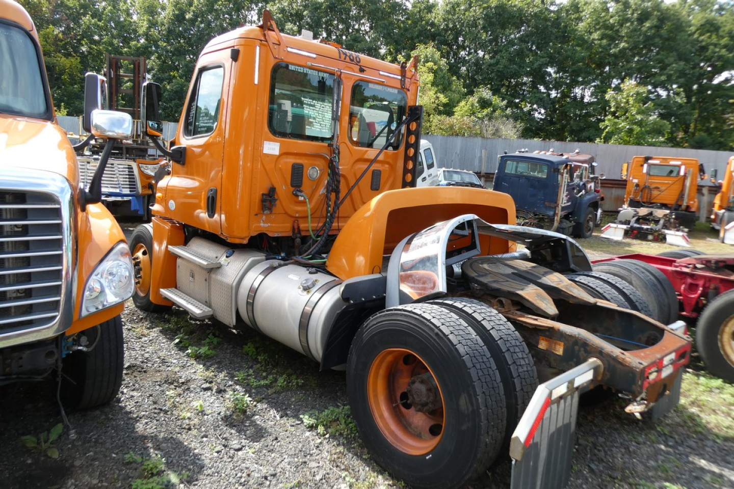 Orange Freightliner Cascadia 125 daycab tractor viewed from side showing cab, fuel tanks, exhaust, and rear frame with dual rear wheels.