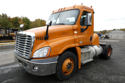 Freightliner Cascadia 125 daycab truck showing orange cab and front grille, with visible wheels and fuel tanks.
