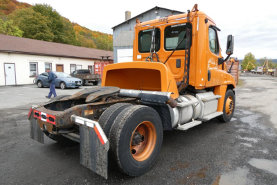 Orange Freightliner Cascadia 125 day cab truck rear view showing hitch, dual rear wheels, and side exhaust. VIN USABLE markings not legible.