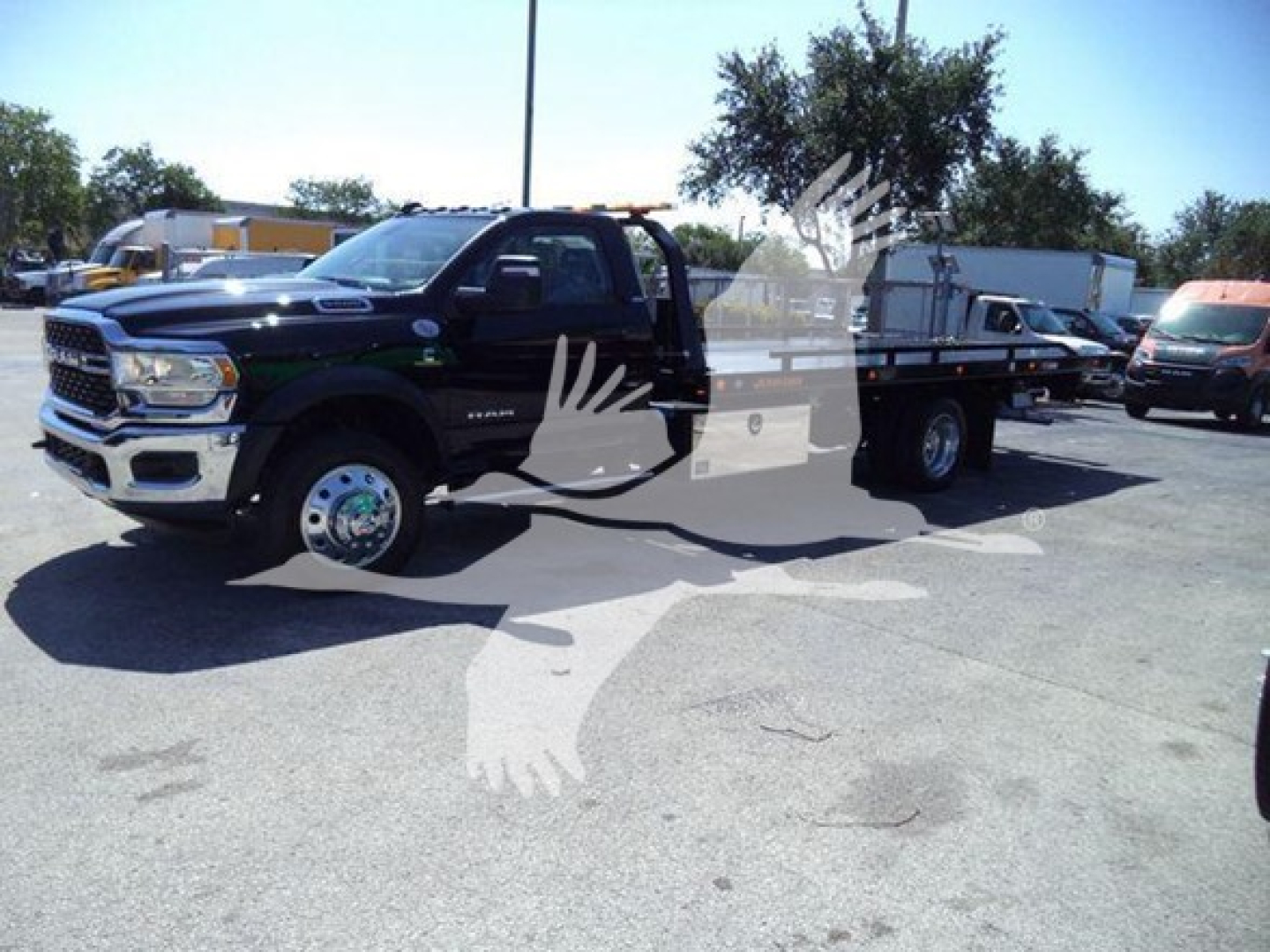 Ram 5500 rollback tow truck in a dealership lot, black extended cab, long flatbed with dual rear wheels, front grille and headlights visible.