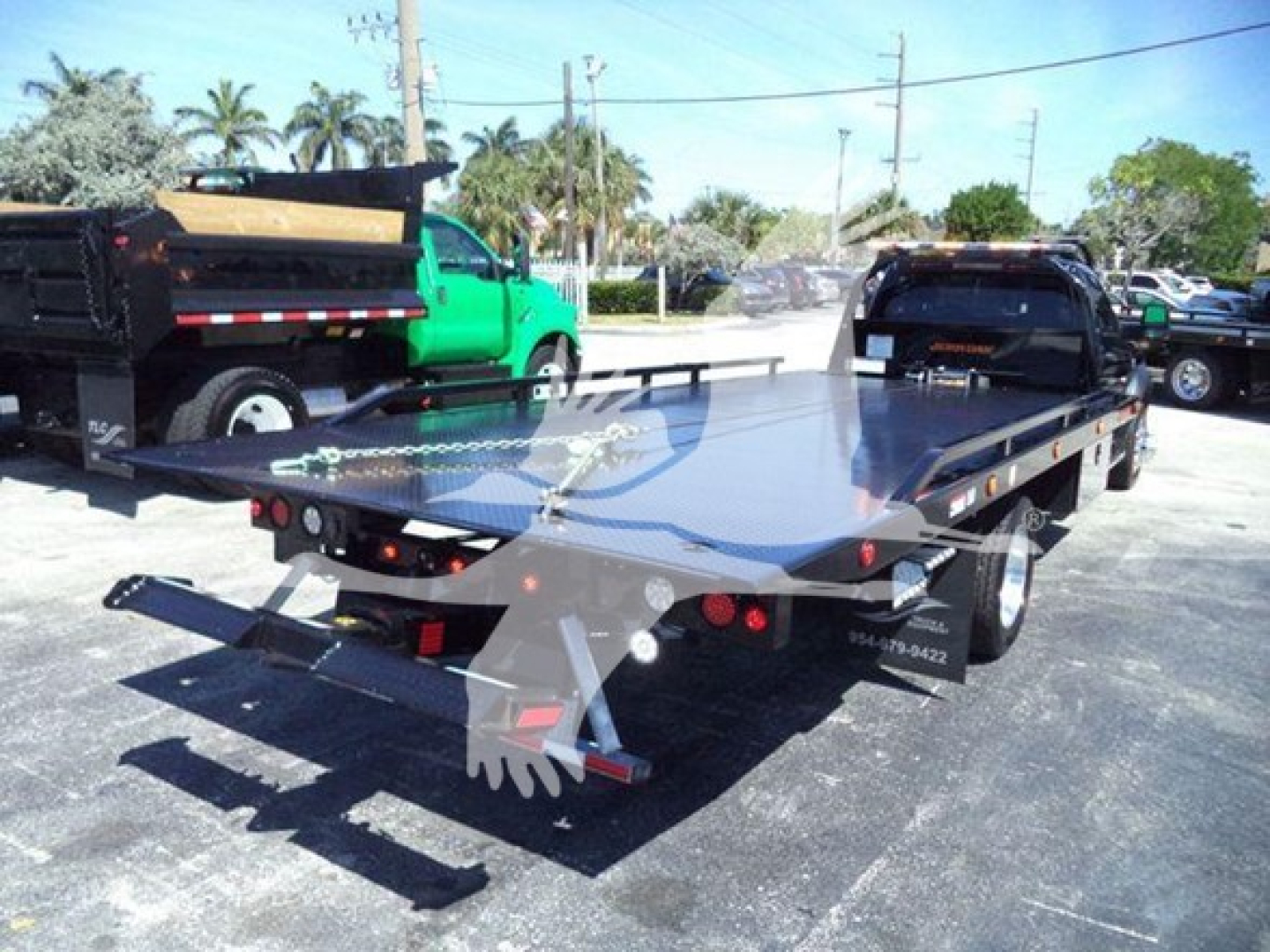 Ram 5500 SLT flatbed rollback tow truck seen from rear-left side, with metal flatbed, lights, and towing equipment.