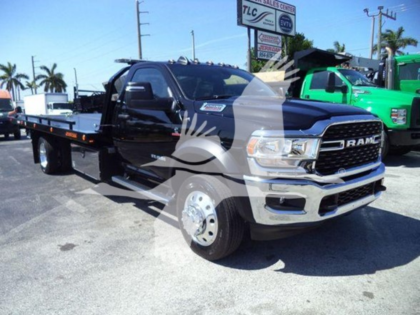 Ram 5500 rollback tow truck front-left view showing flatbed with chrome grille and dual rear wheels, black cab, dealership lot in background.