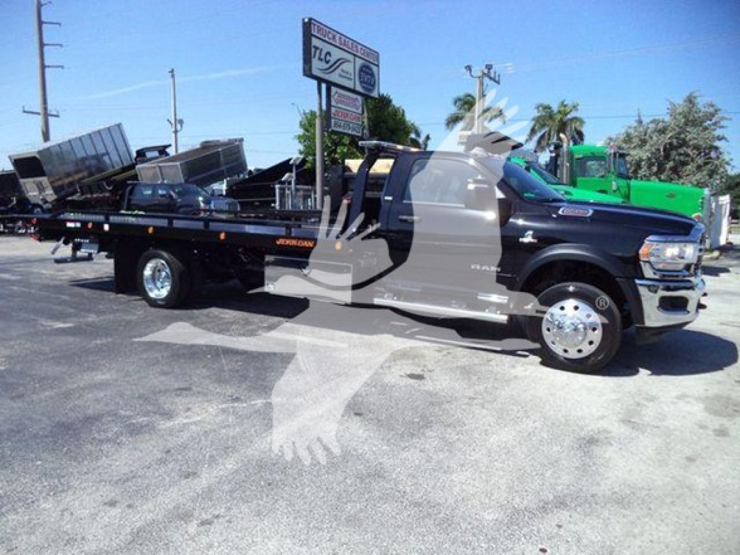 Ram 5500 SLT rollback tow truck in a dealership lot with a flatbed and equipment on it, showing side profile and front wheel.