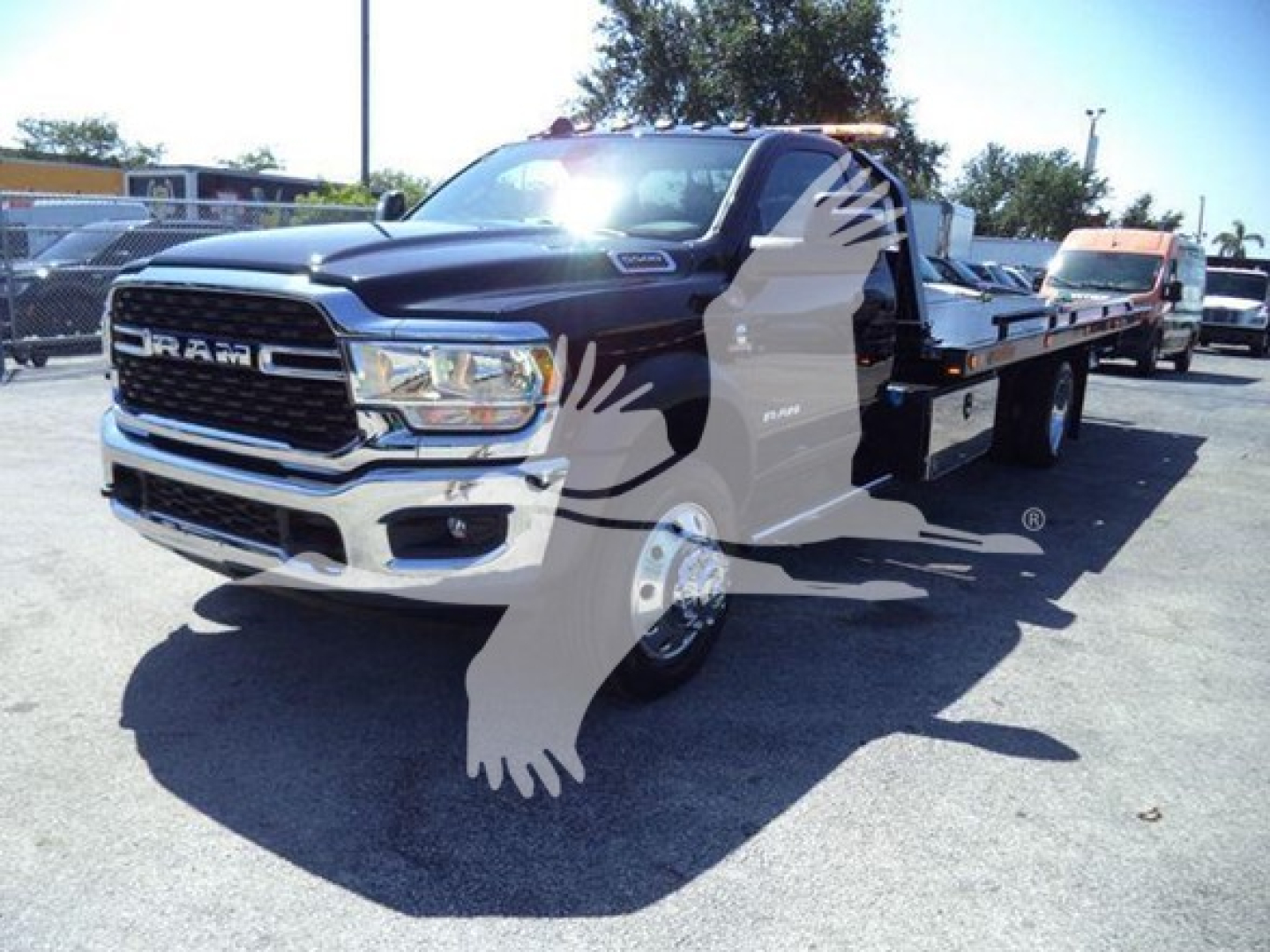 Ram 5500 truck in a dealership lot, front grille with RAM emblem, 'RAM' lettering on grille, white and black color, rollback tow truck chassis visible in background.
