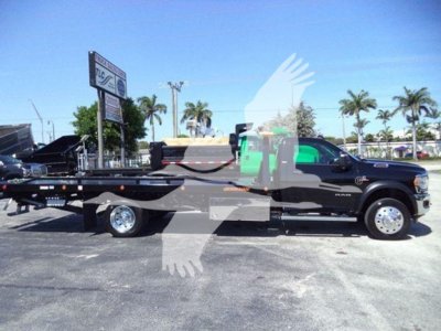 Ram 5500 SLT truck with rollback bed in serviceable condition, side view showing long flatbed and dual rear wheels, dealership lot in background.