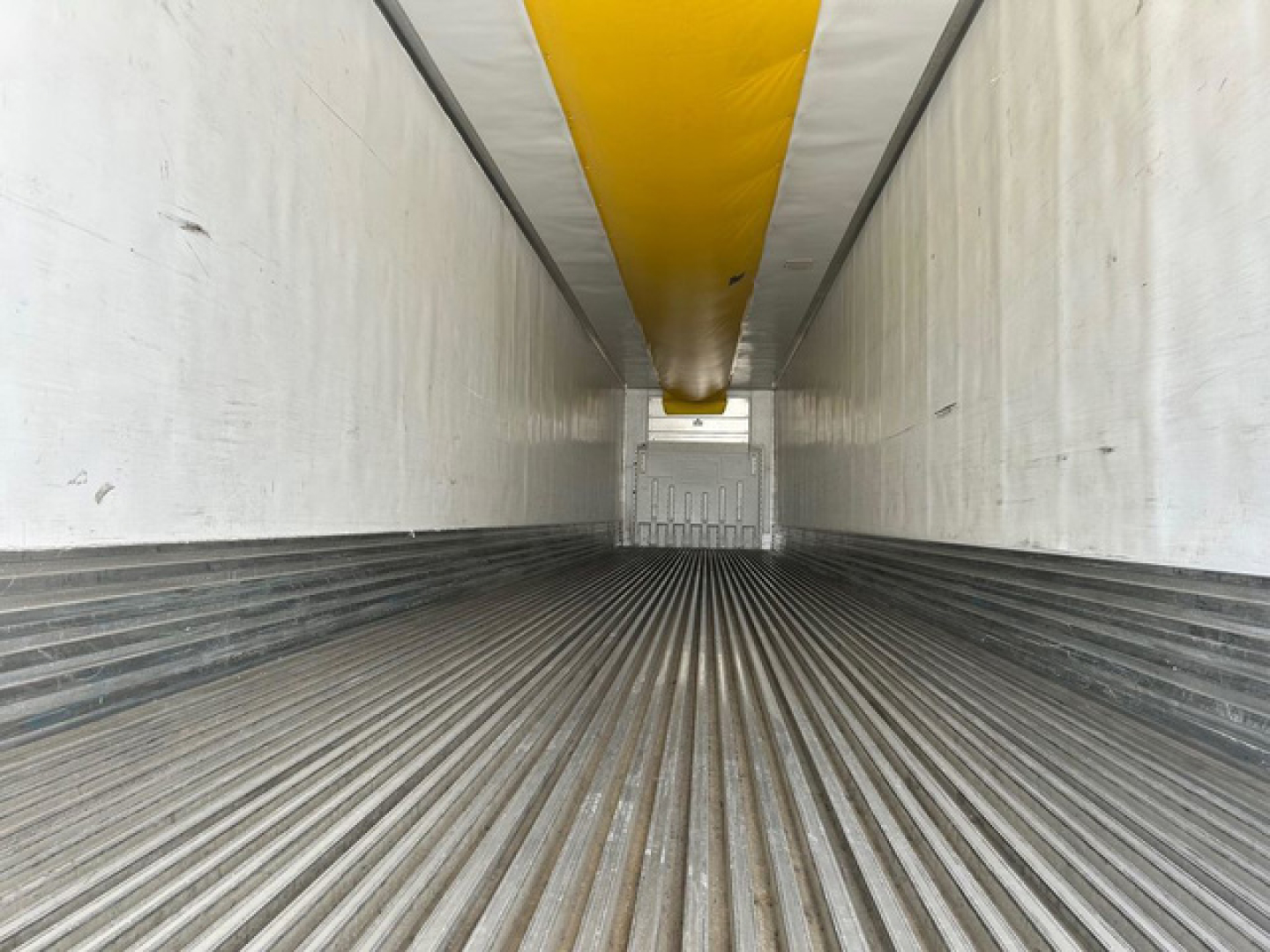Trailer cargo area view inside a 2019 Utility Reefer showing ribbed metal floor, white interior walls, and a yellow overhead component.