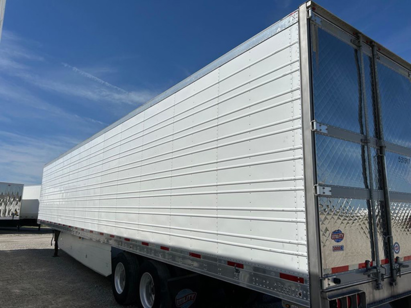 Utility reefer trailer side view showing white aluminum cargo area and tandem axle with rear doors; no visible text on the side.