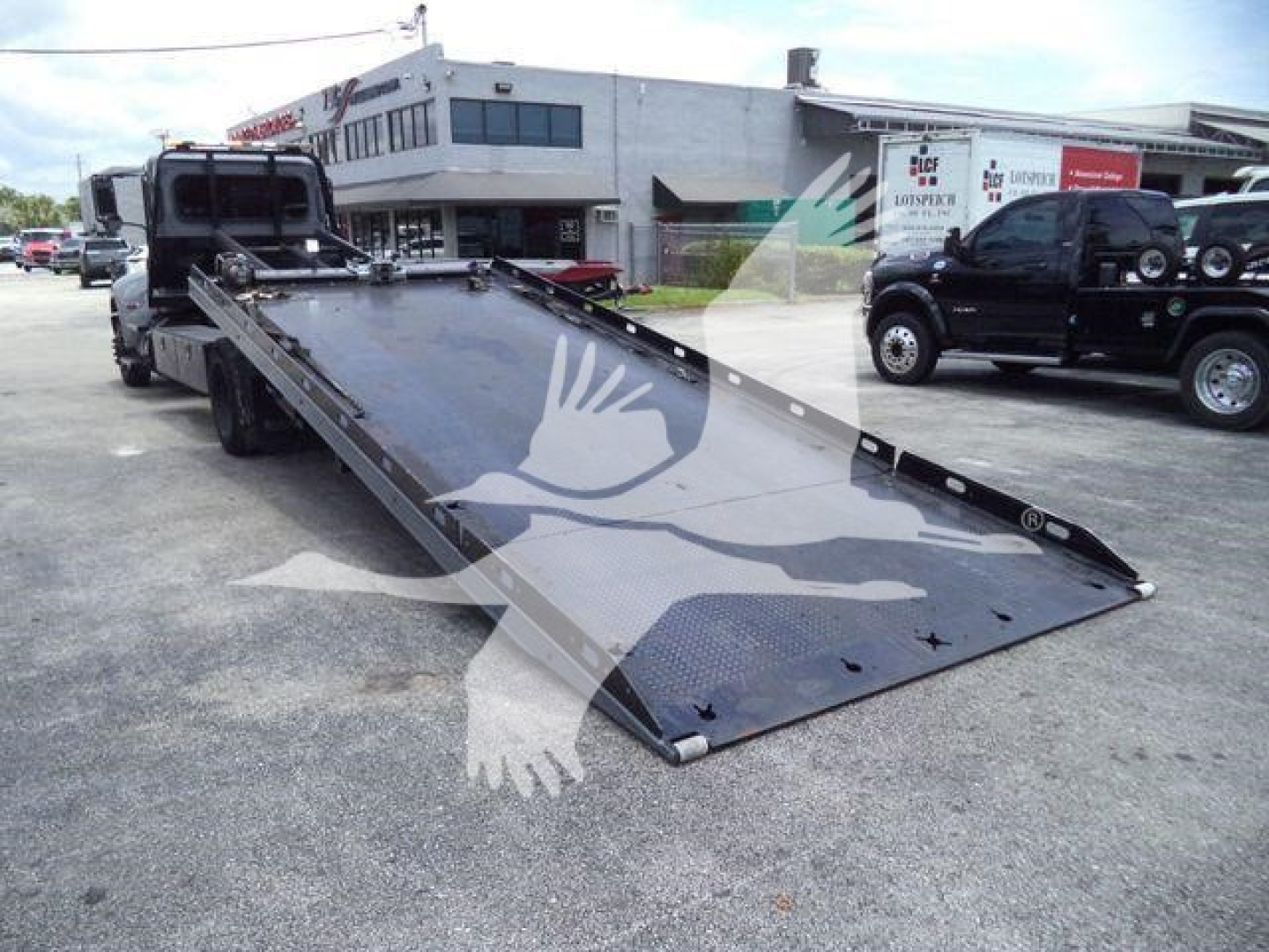 Peterbilt 337 rollback tow truck with long black metal ramp extended in front, service shop background, VIN plate not visible.
