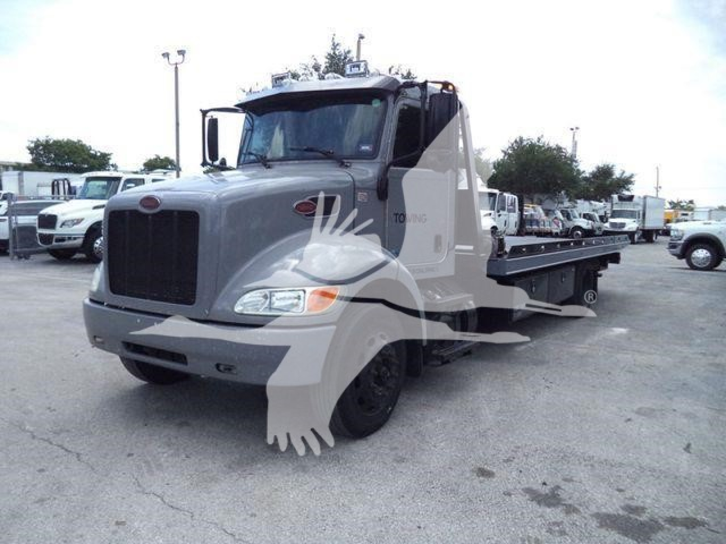 2021 Peterbilt 337 rollback truck in a parking lot, cab, front grille, and flatbed with wheel marks and light reflection