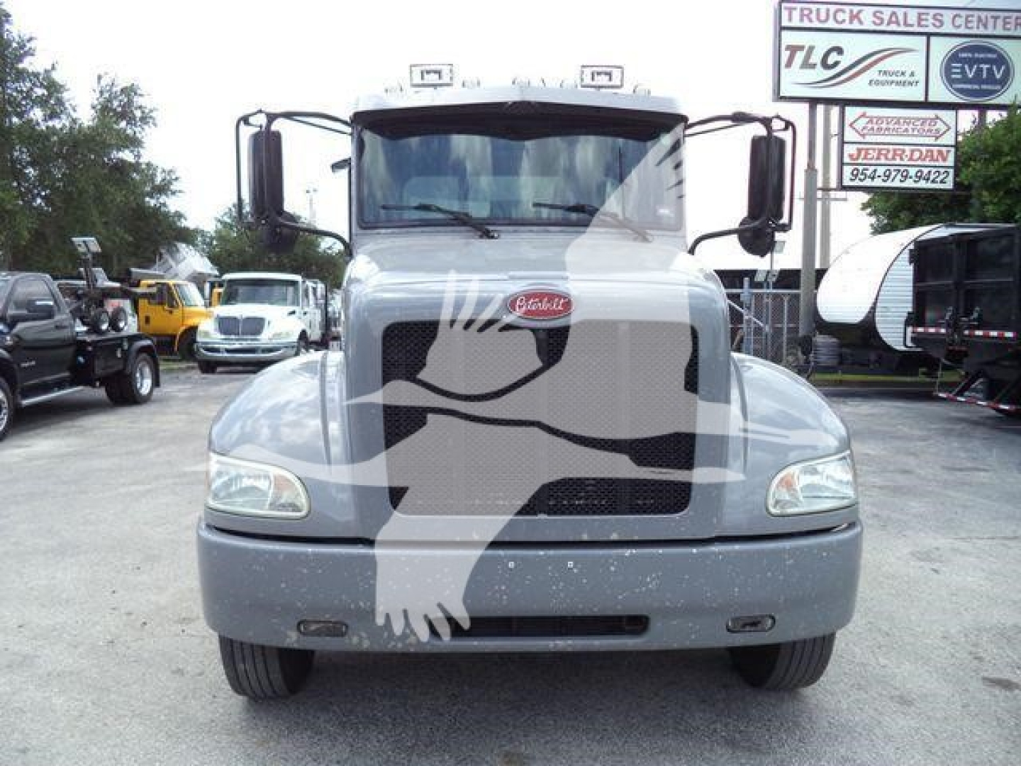 Front view of a 2021 Peterbilt 337 rollback truck showing Peterbilt emblem on grille and large windshield; surroundings include dealership lot and signage in background.