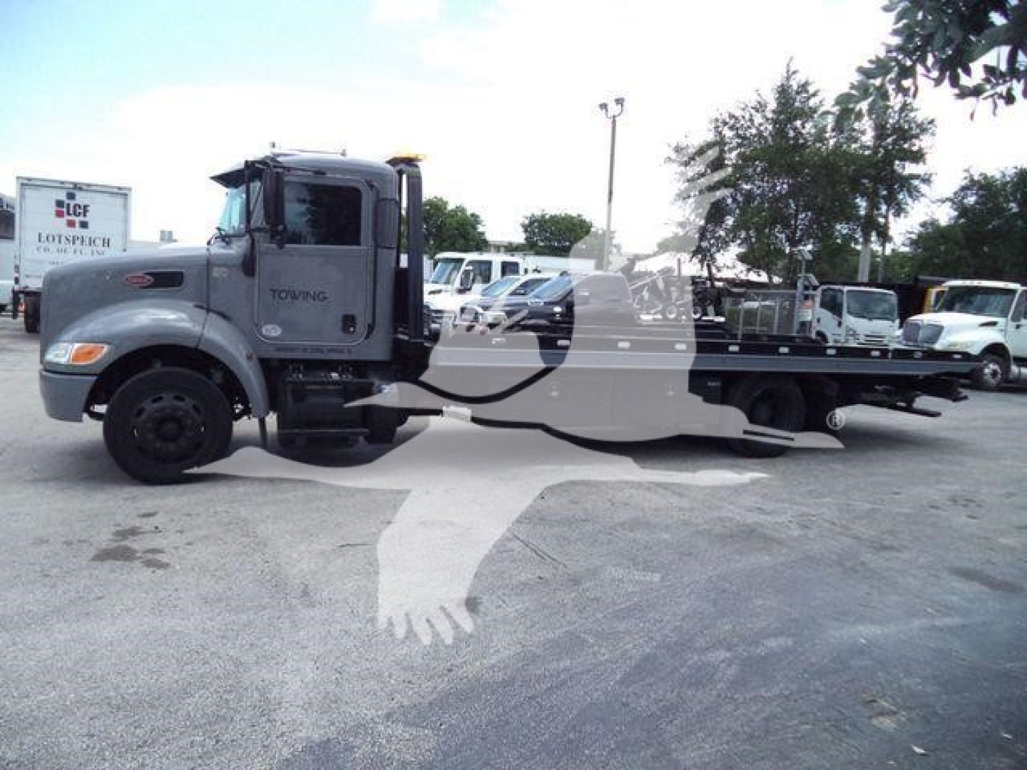 Peterbilt 337 rollback truck side view showing cab and long flatbed, gray color, with towing branding on door.