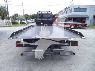 Peterbilt 337 rollback bed rear view showing flatbed with rear bumper, taillights, and towing link; visible factory markings and a vehicle yard in background.