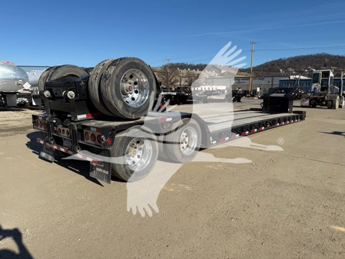 Trailer lowboy flatbed showing dual rear axles and spare tires mounted on a trailer deck.