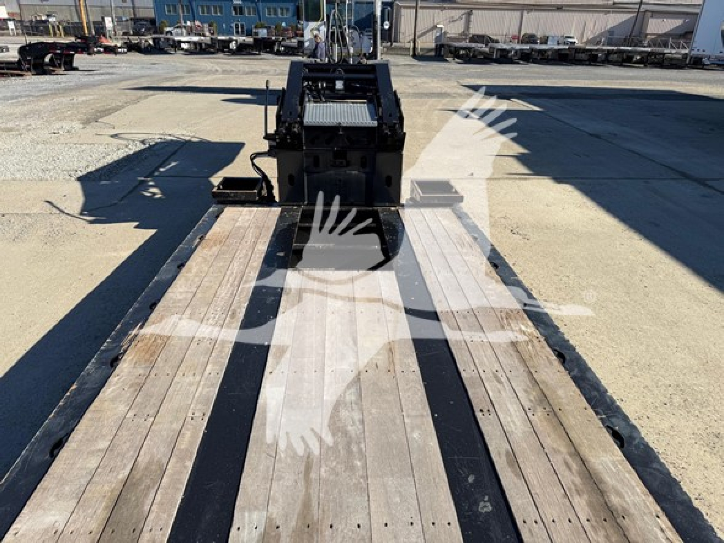 Trailer deck of a lowboy trailer showing wooden planks and gooseneck hitch area, with metal framework and loading ramps in the background.