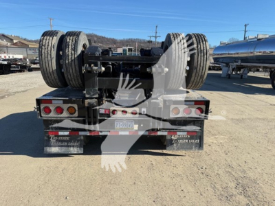 Trailer rear view showing dual rear axles with heavy tires and mud flaps, lights, and license plate area; steel frame and deck components visible.