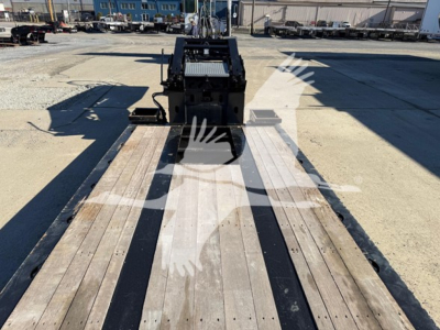 Trailer deck of a lowboy trailer showing wooden planks and gooseneck hitch area, with metal framework and loading ramps in the background.