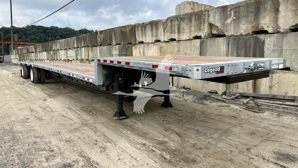 Manac steel drop deck trailer showing low-profile landing gear and front gooseneck area with Legend branding on the rear.