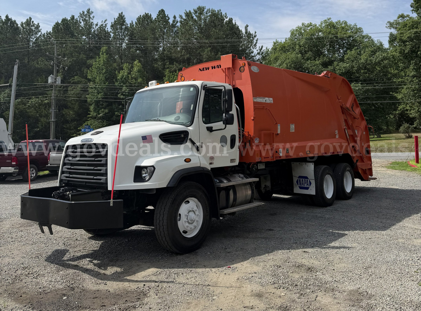 Truck showing a Freightliner 114SD garbage body with white cab and orange rear compactor, front view in a gravel lot.