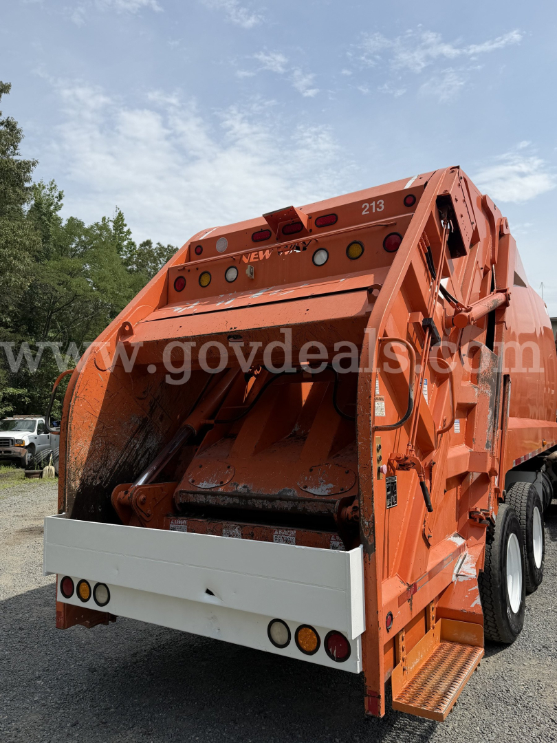 Rear view of an orange Freightliner diesel truck garbage body with rear bumper and wheels visible.