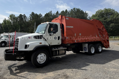 Truck showing a Freightliner 114SD rear hopper garbage body with white cab and orange container, side view with branding and VIN/stock details not visible on the image.