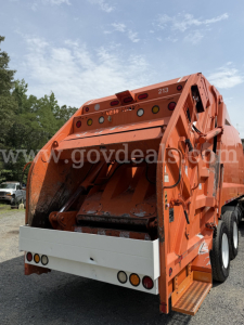 Rear view of an orange Freightliner diesel truck garbage body with rear bumper and wheels visible.