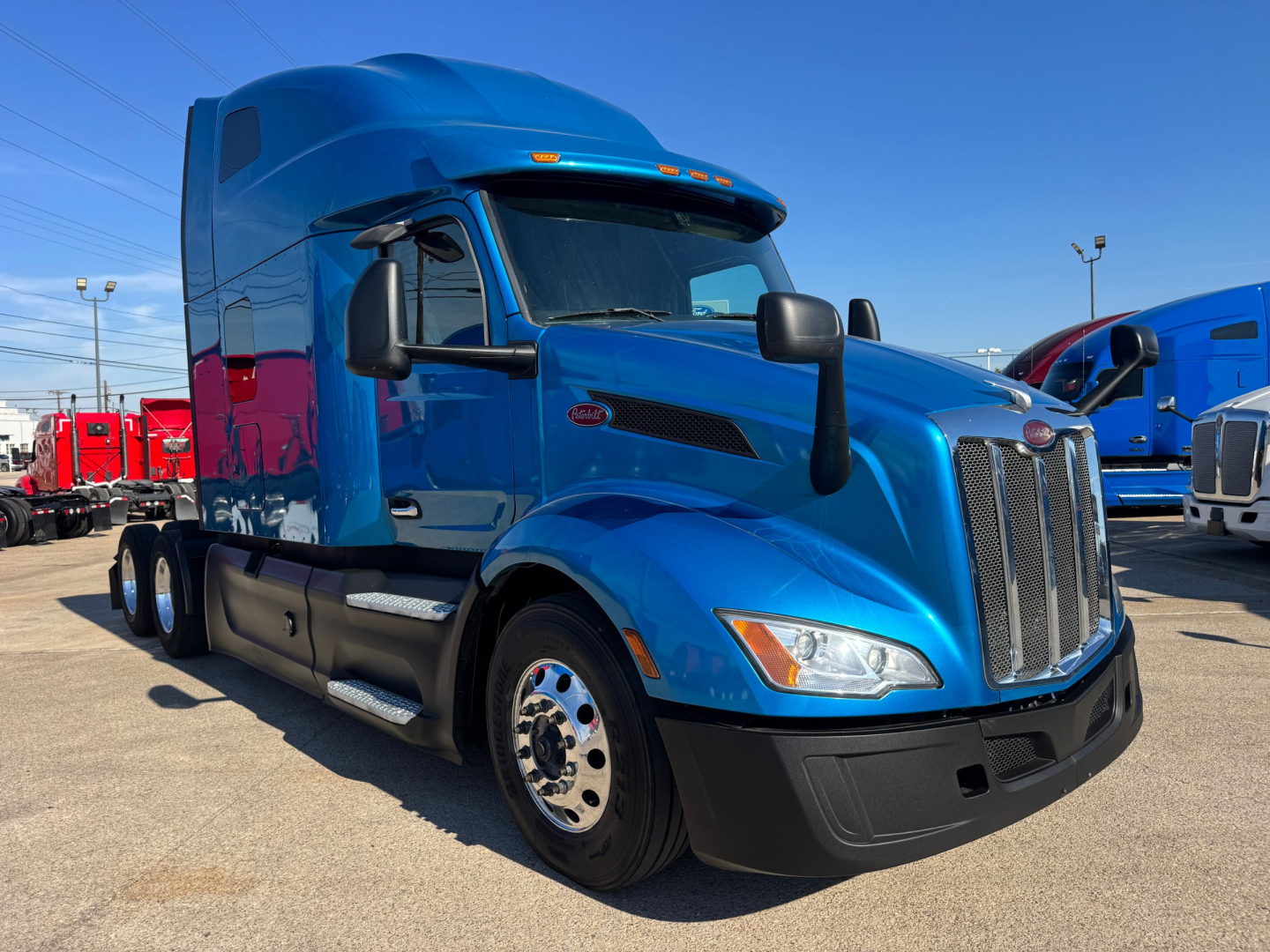 Blue 2023 Peterbilt 579 conventional sleeper truck in a dealership lot, front three-quarter view, showing large grille, aerodynamic hood, and dual rear wheels.