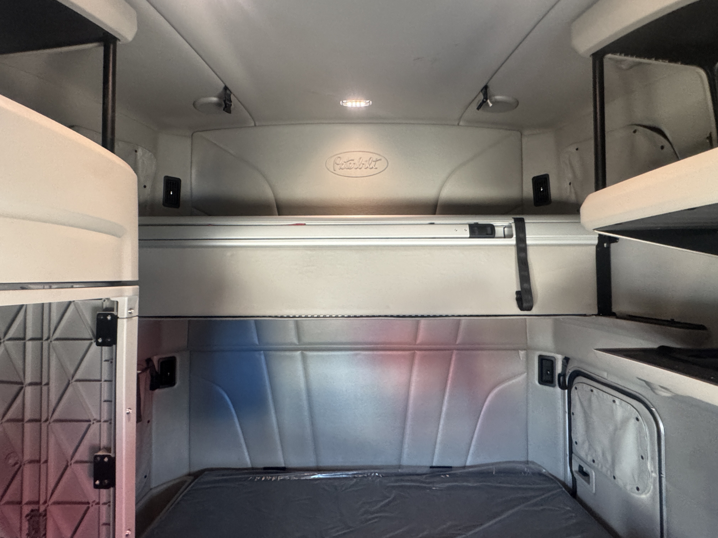 Peterbilt sleeper cab interior with bunk area visible; upper berth rails and storage, metal divider, light, and cargo floor.