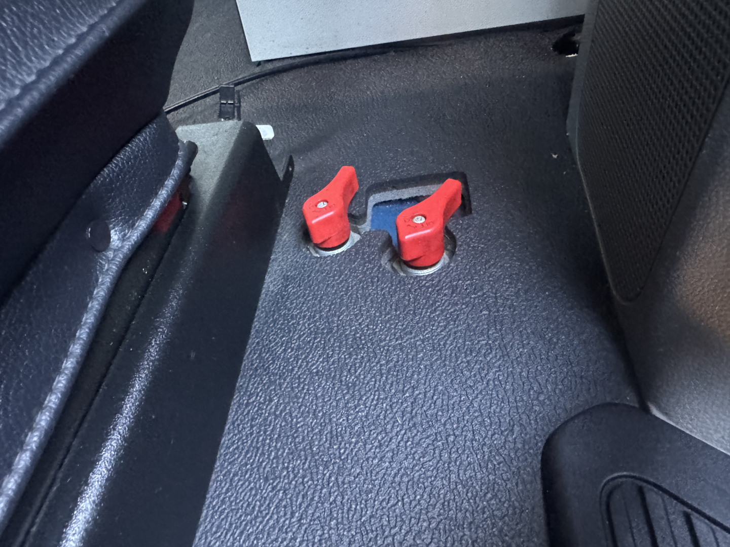 Peterbilt 579 interior showing two red toggle latches on a blue slider area, with black floor and seats nearby.