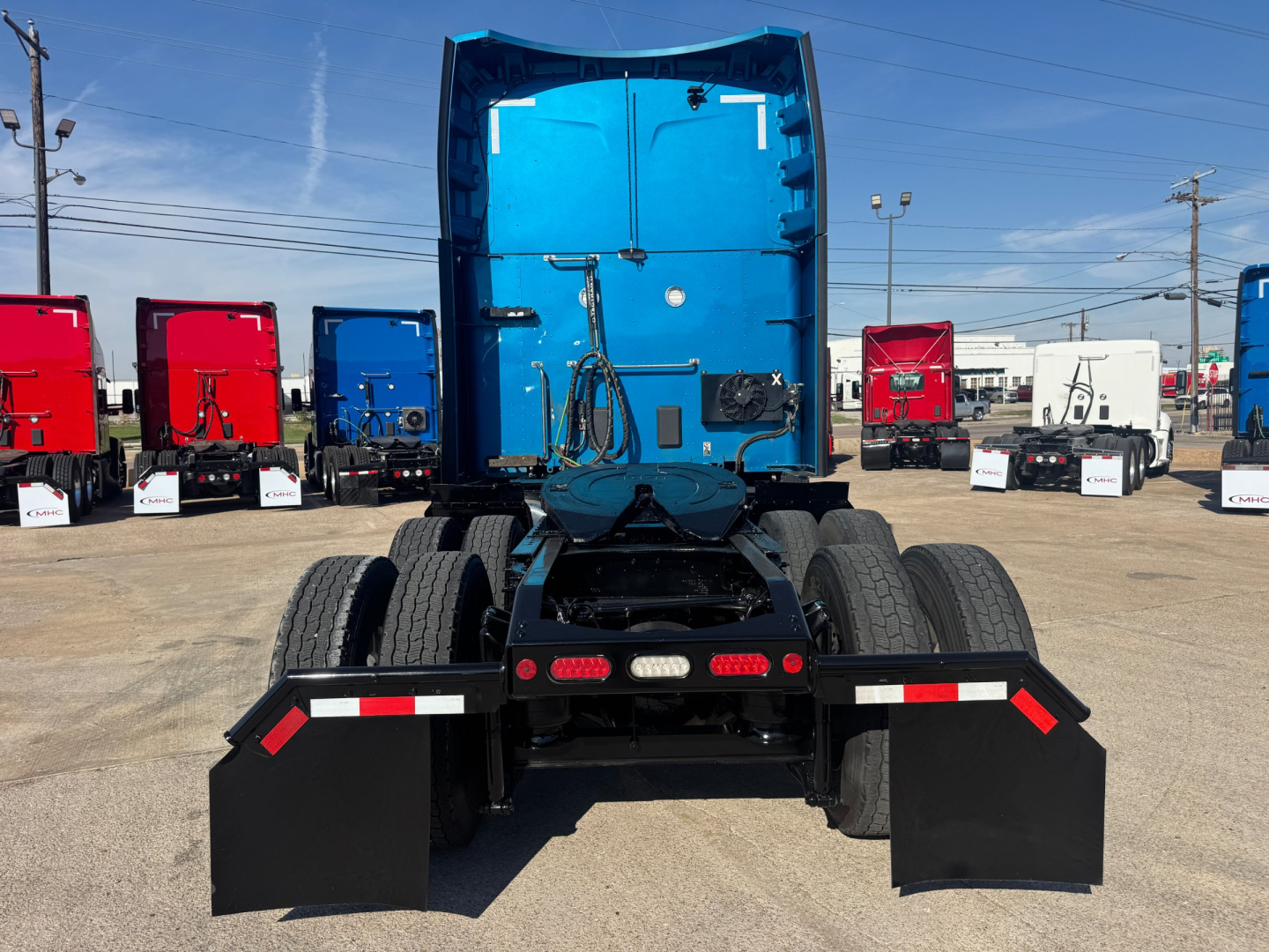 Peterbilt 579 tractor rear view showing blue sleeper cab, dual rear axles, and mudflaps; various trailers in background.